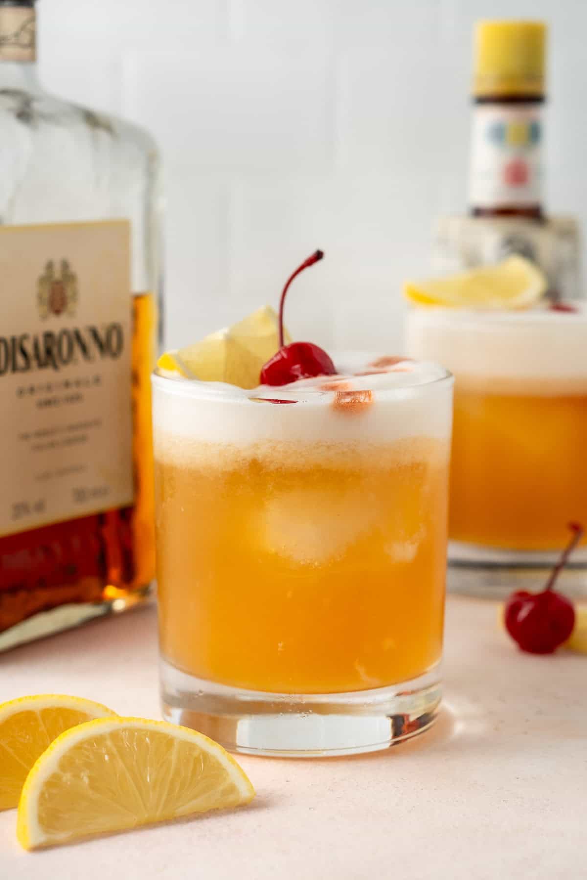 Close up of an amaretto sour cocktail garnished with a cherry and lemon wedge.