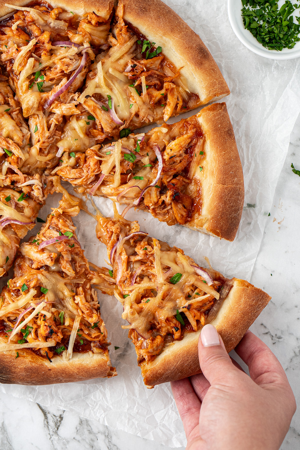 A hand pulling a slice of BBQ chicken pizza.