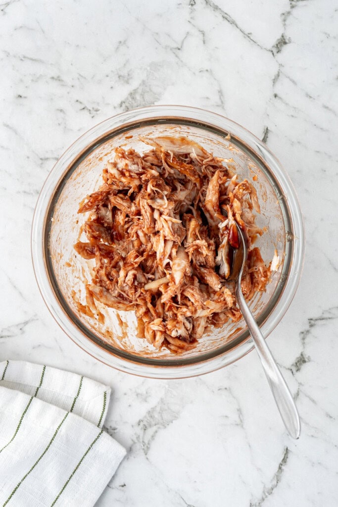 Mixing the shredded chicken with BBQ sauce in a small glass bowl.