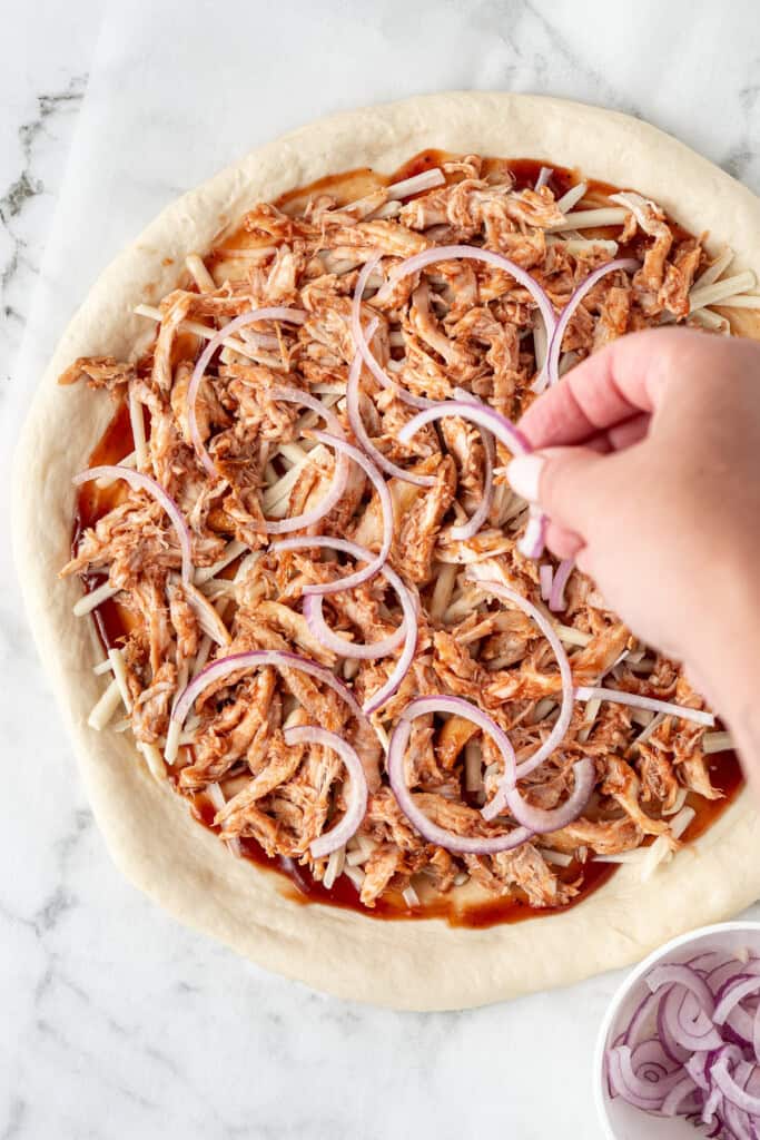 Adding sliced red onion to the pizza.