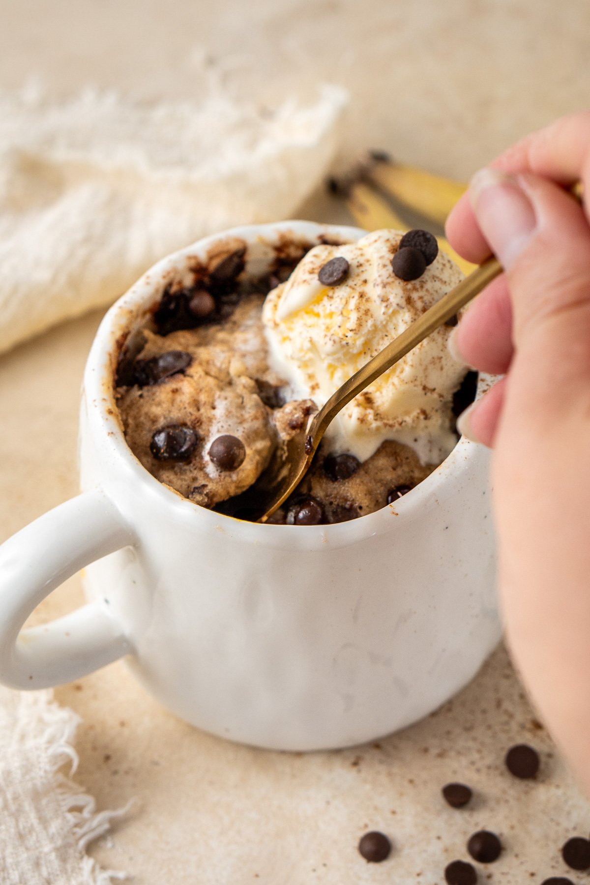 A hand with a spoon scooping a bite of banana bread mug cake with ice cream.