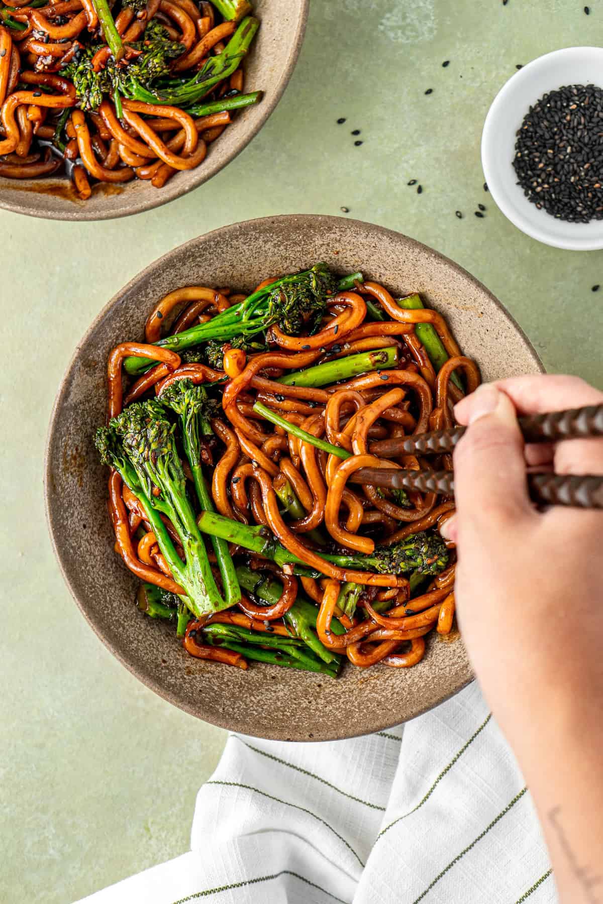 A hand taking a bite of garlic chilli udon noodles with chopsticks.