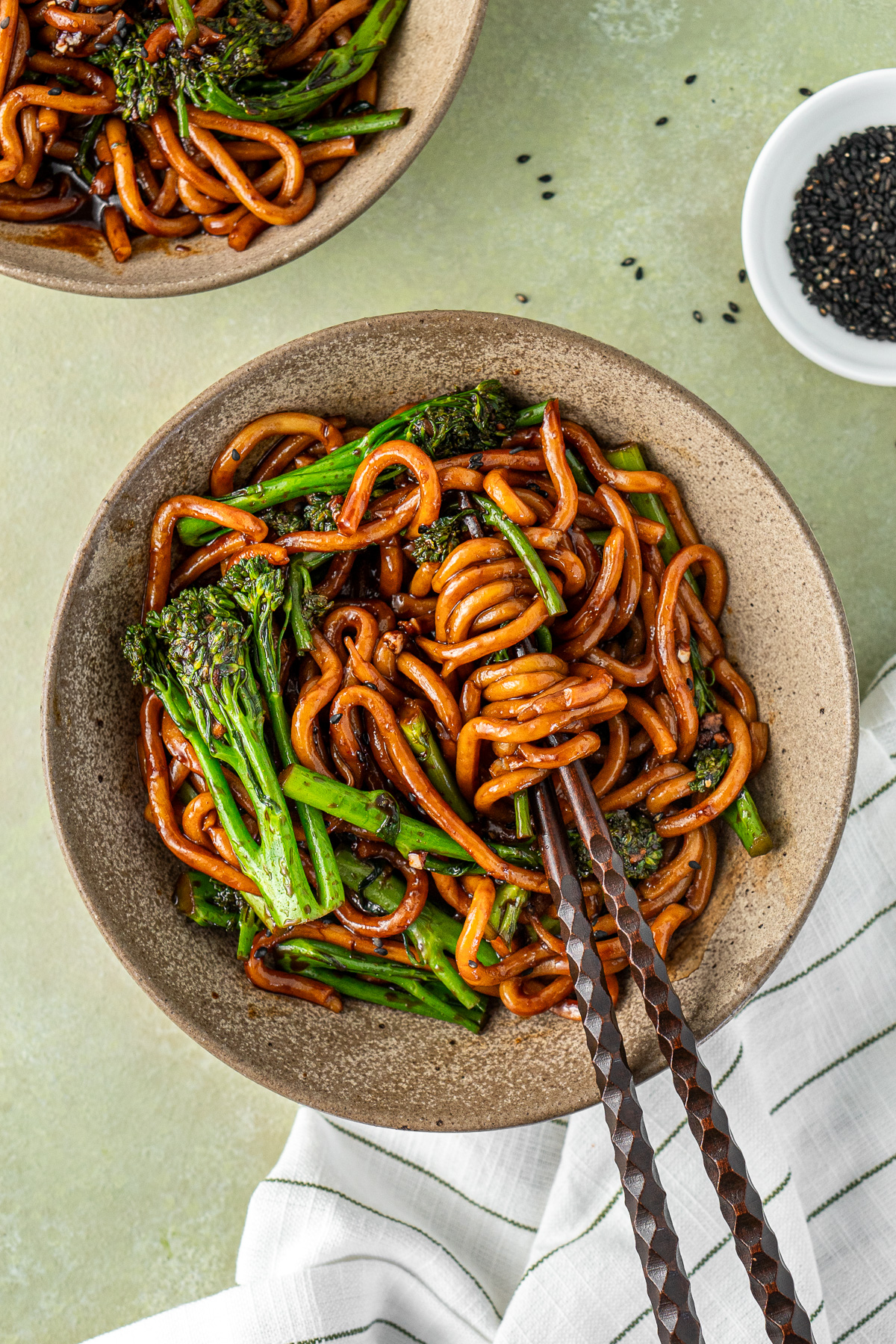 A bowl of chilli garlic udon noodles with broccolini with chopsticks.