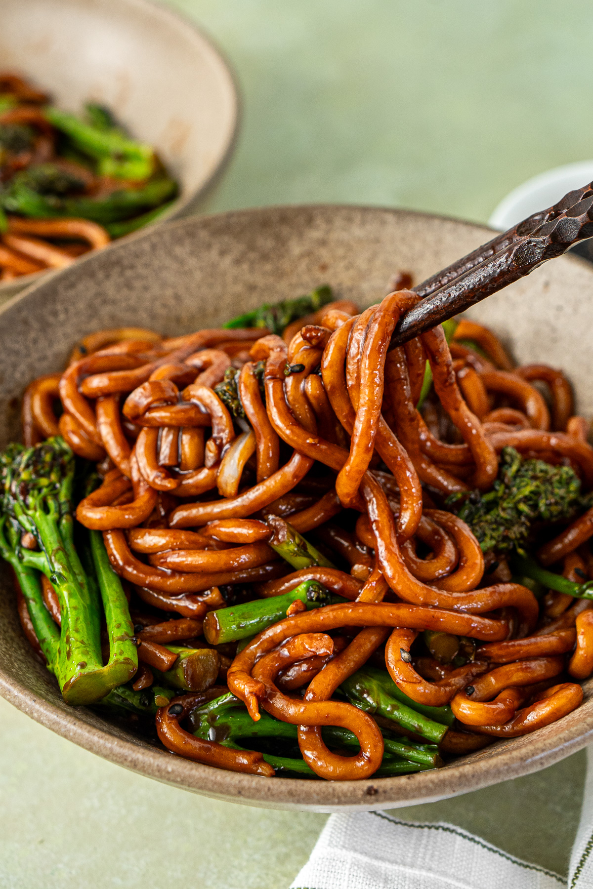 Chopsticks pulling out a bite of saucy udon noodles.