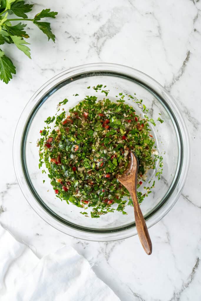 The mixed chimichurri in a glass bowl.