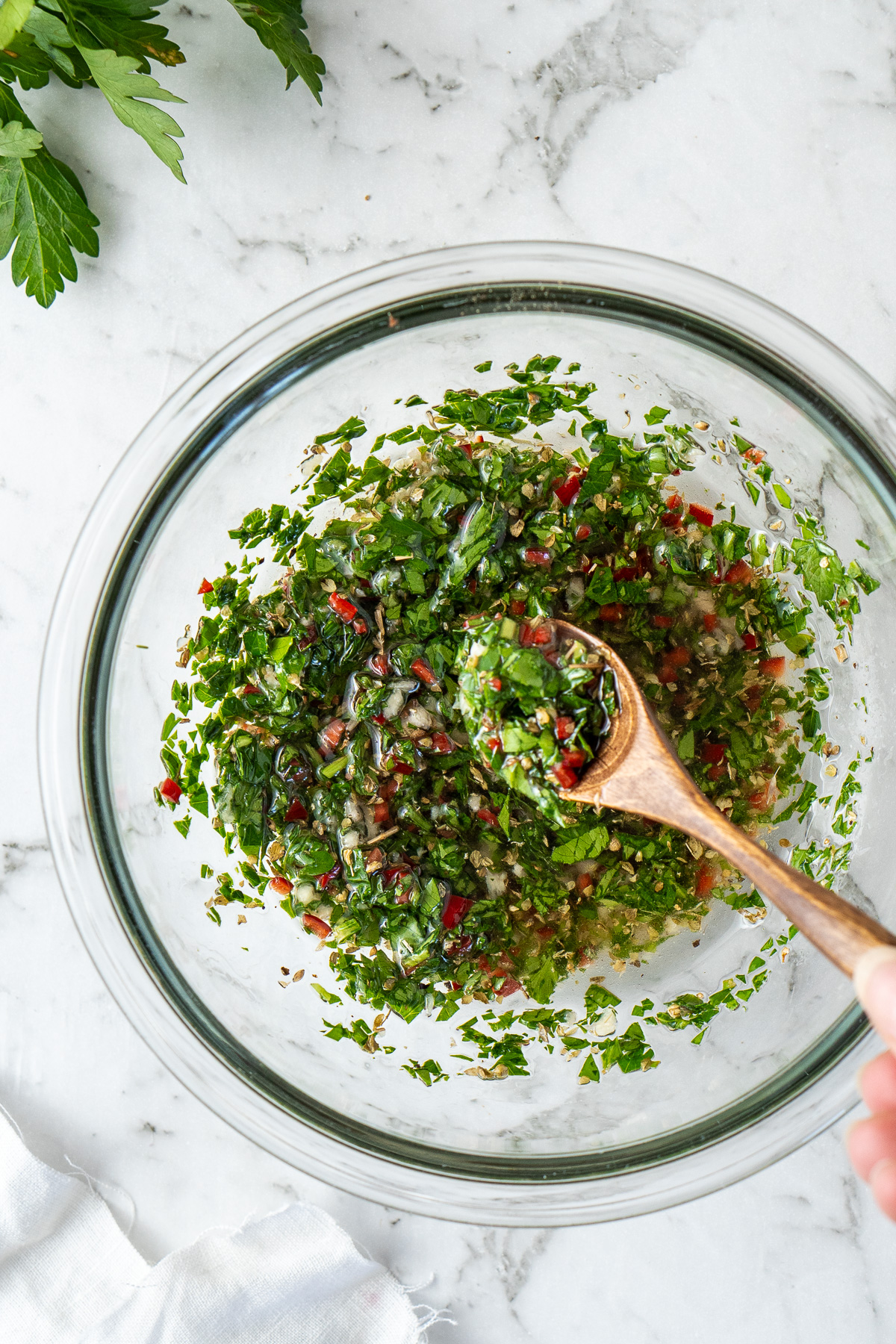 Close up of a spoon taking some of the chimichurri from a glass bowl.