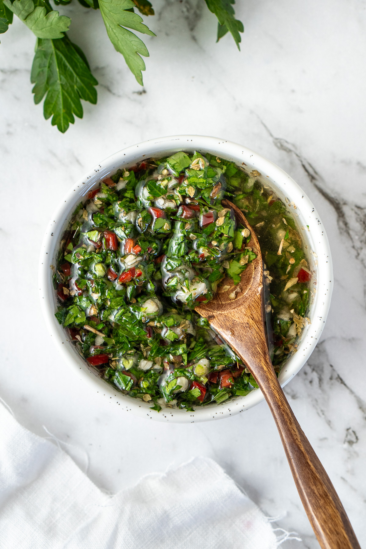 Close up of a wooden spoon in a bowl of chimichurri. 