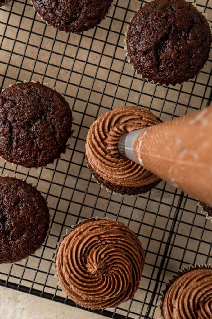 Piping buttercream onto cupcakes.