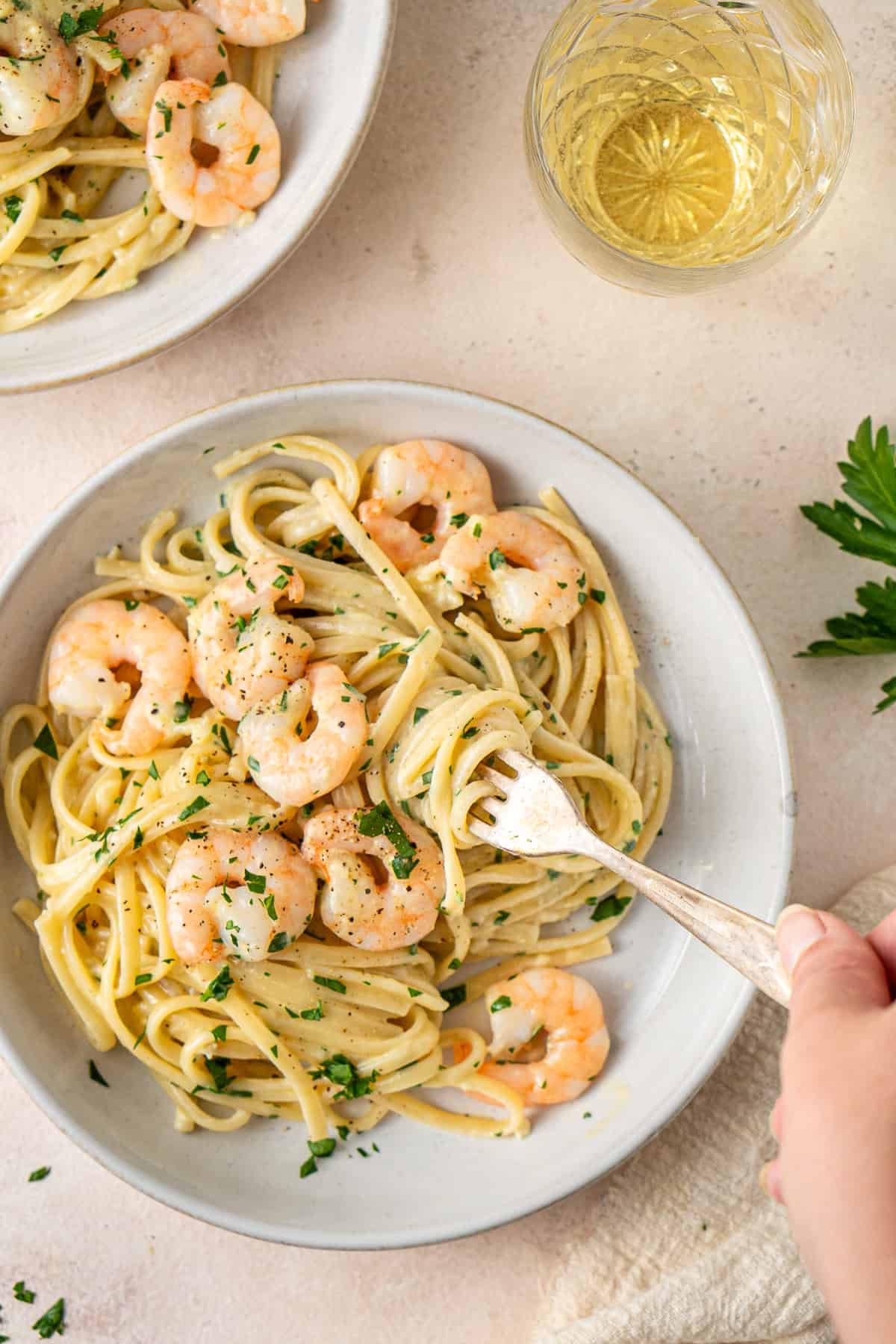 A hand using a fork to twirl the creamy garlic pasta. 