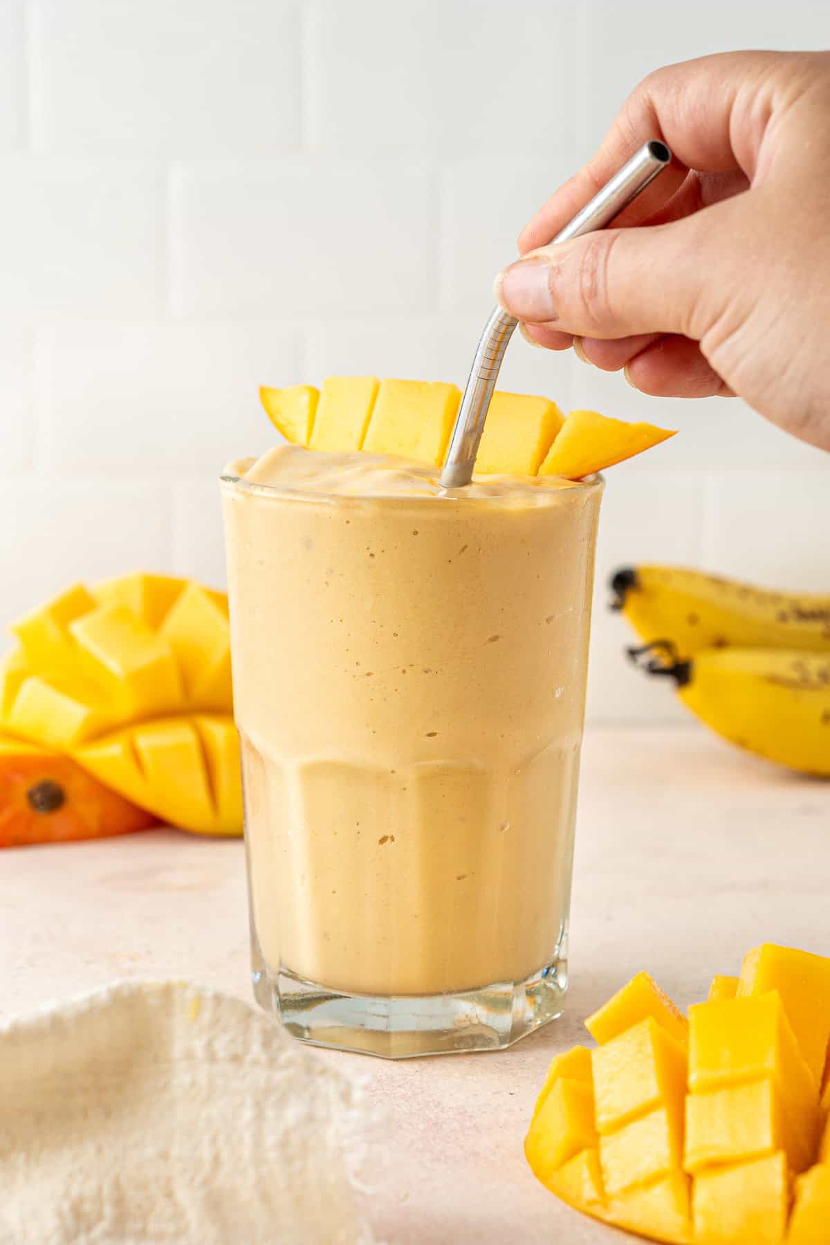 A hand putting a straw into a dairy free mango smoothie.