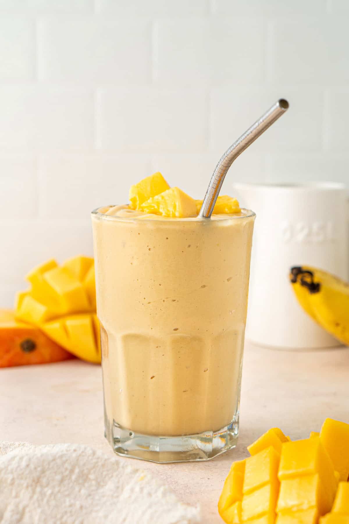 Close up of a dairy free mango smoothie in a glass with a metal straw.