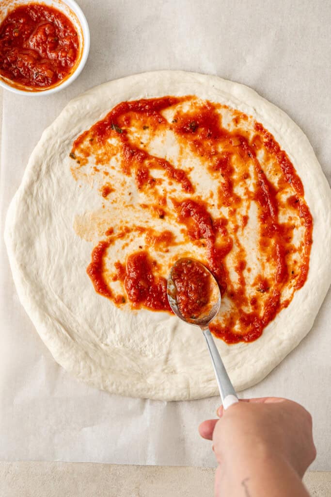 Spreading pizza sauce onto the base.