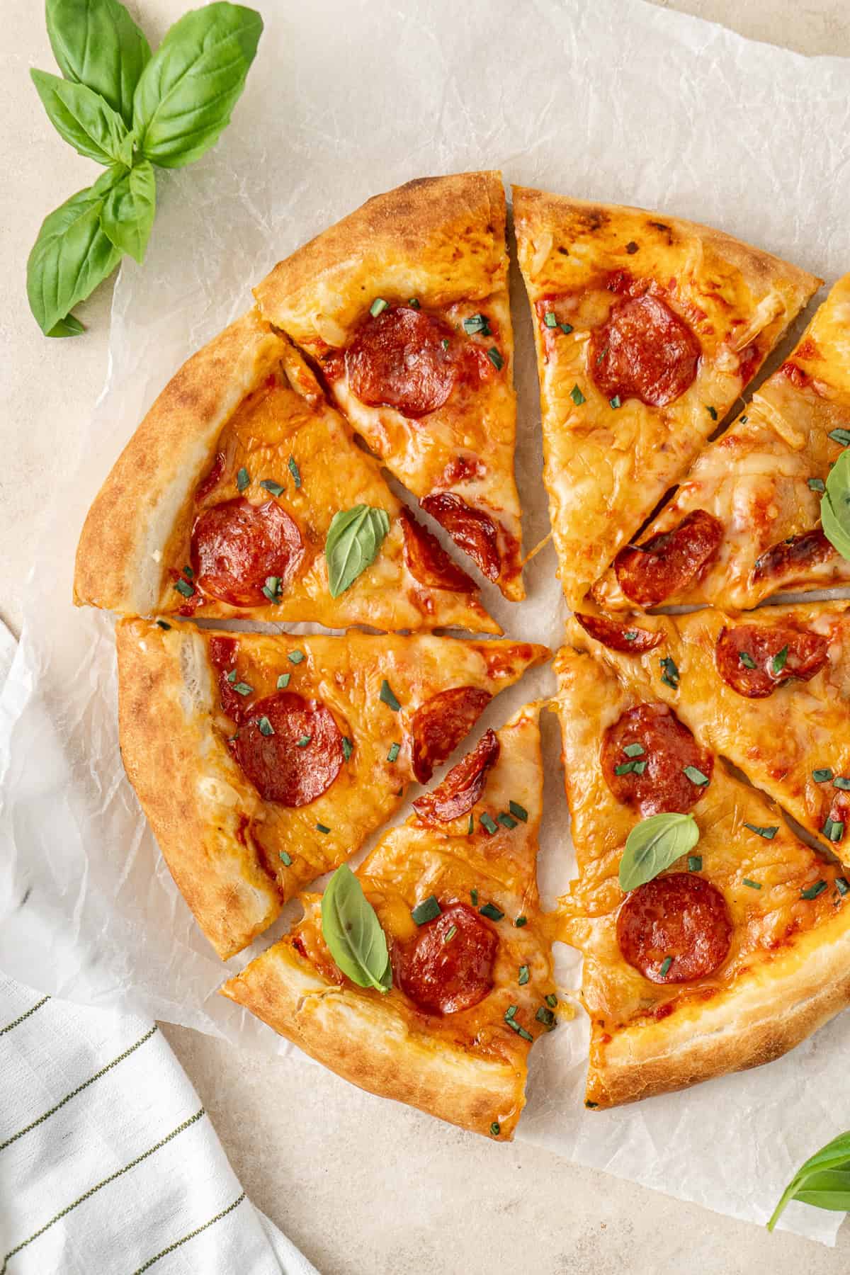 Close up of a sliced dairy free pizza with pepperoni and fresh basil.