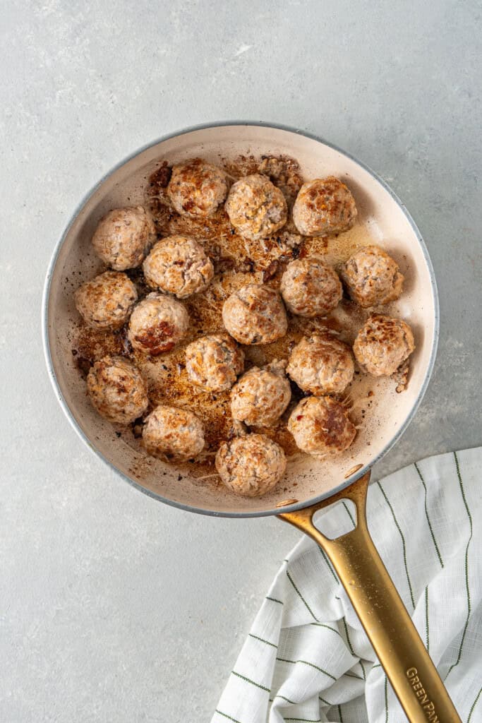 The browned pork meatballs in a frying pan.