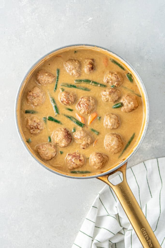 The finished green curry meatballs in the curry sauce in the frying pan.