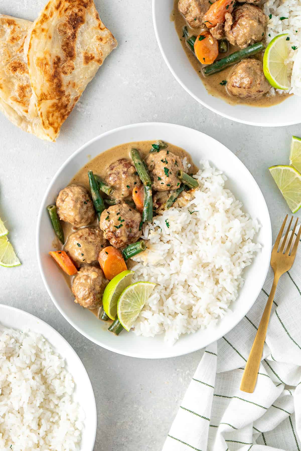 Green curry meatballs served into white bowls with rice and lime wedges. 