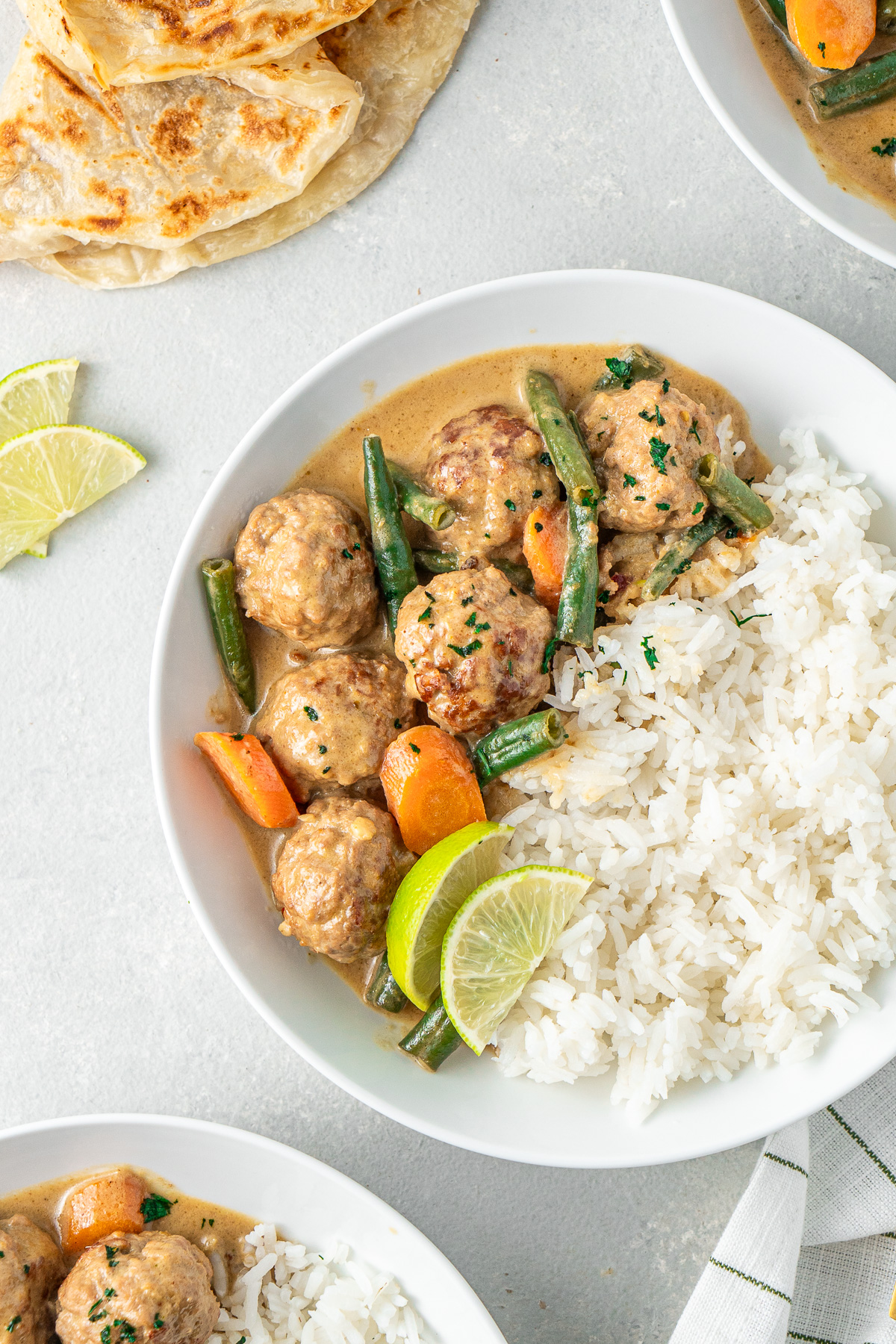 Close up of pork meatballs in a green curry sauce served over rice.