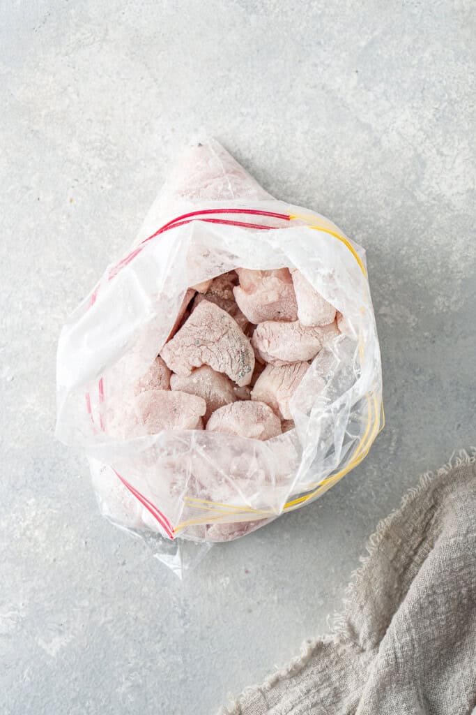 The pieces of chicken coated in corn flour in a zip lock bag.