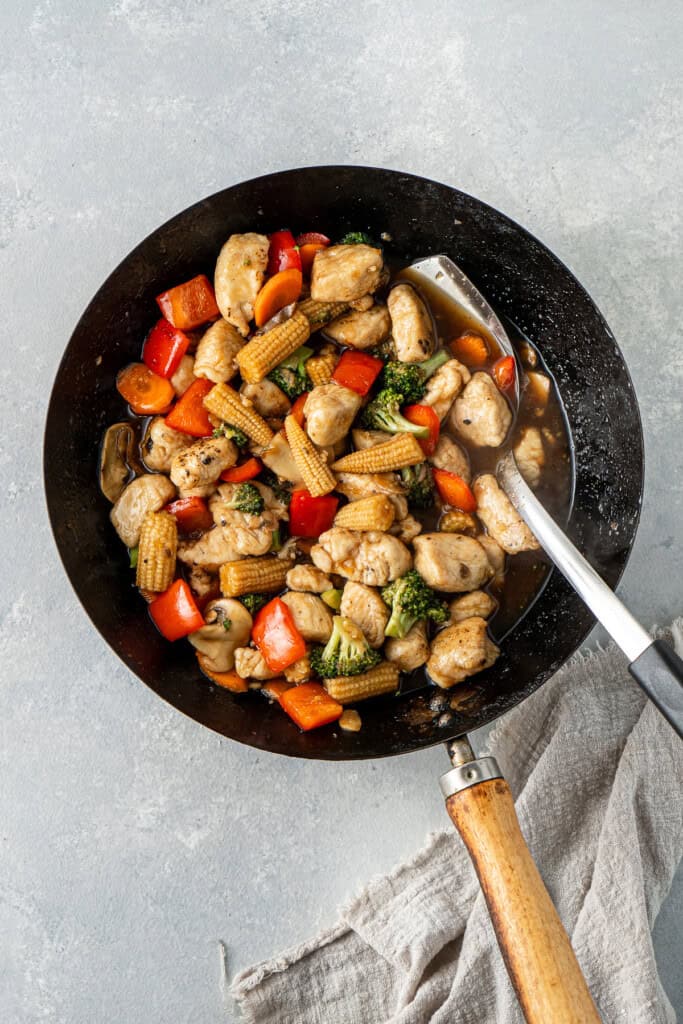 The chicken and vegetable stir fry in the sauce in a wok.