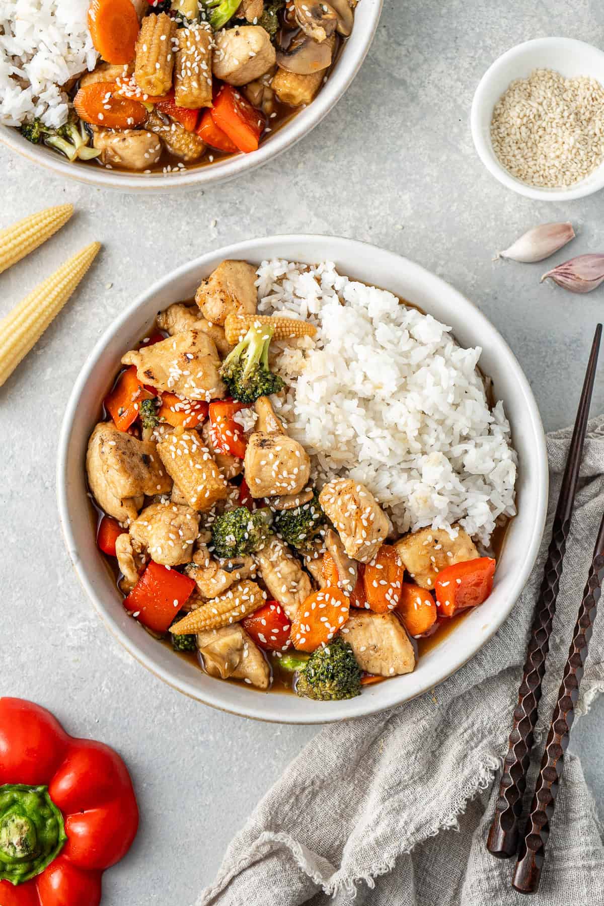 Honey garlic chicken and vegetable stir fry served in bowls with rice and topped with sesame seeds.