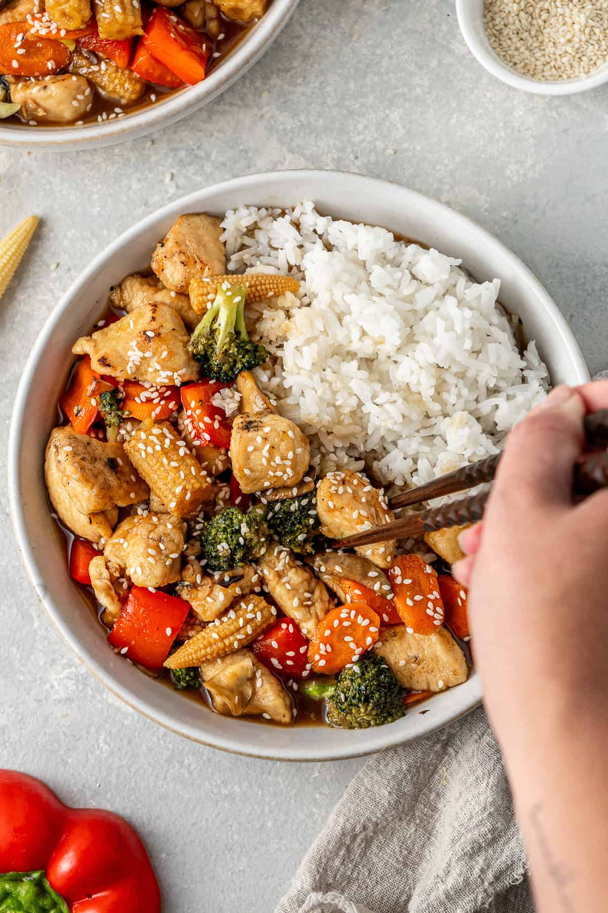 Close up of a hand using chopsticks to pick up a piece of chicken from the stir fry.