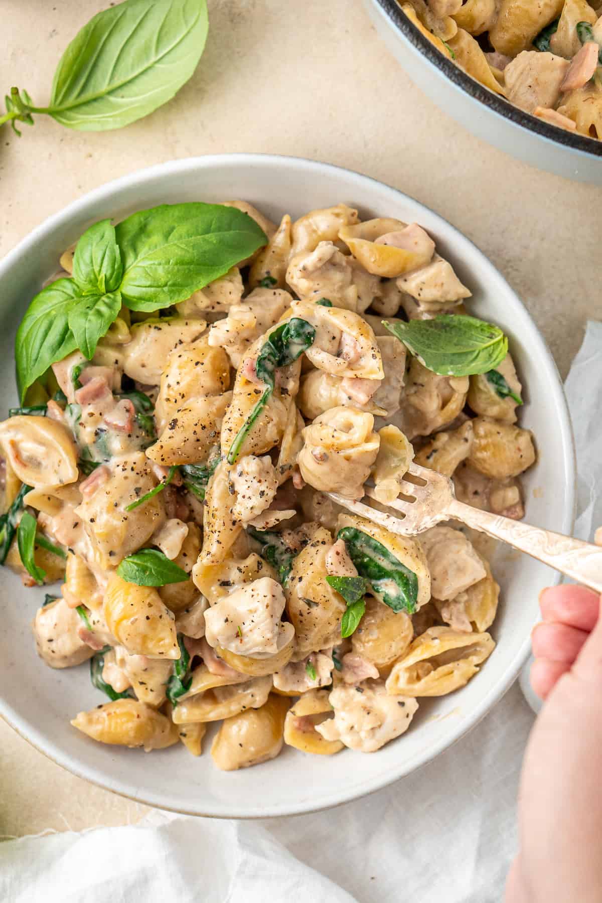 Close up of a fork taking a bite of creamy chicken and bacon pasta.