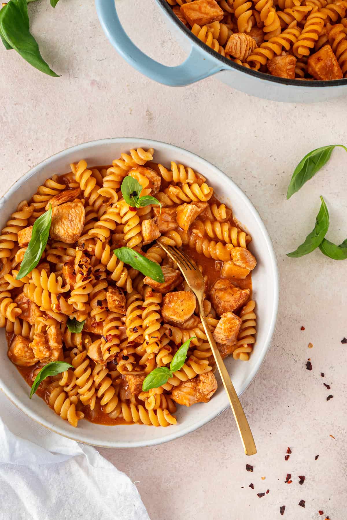 A fork taking a bite from a bowl of creamy chicken tomato pasta.