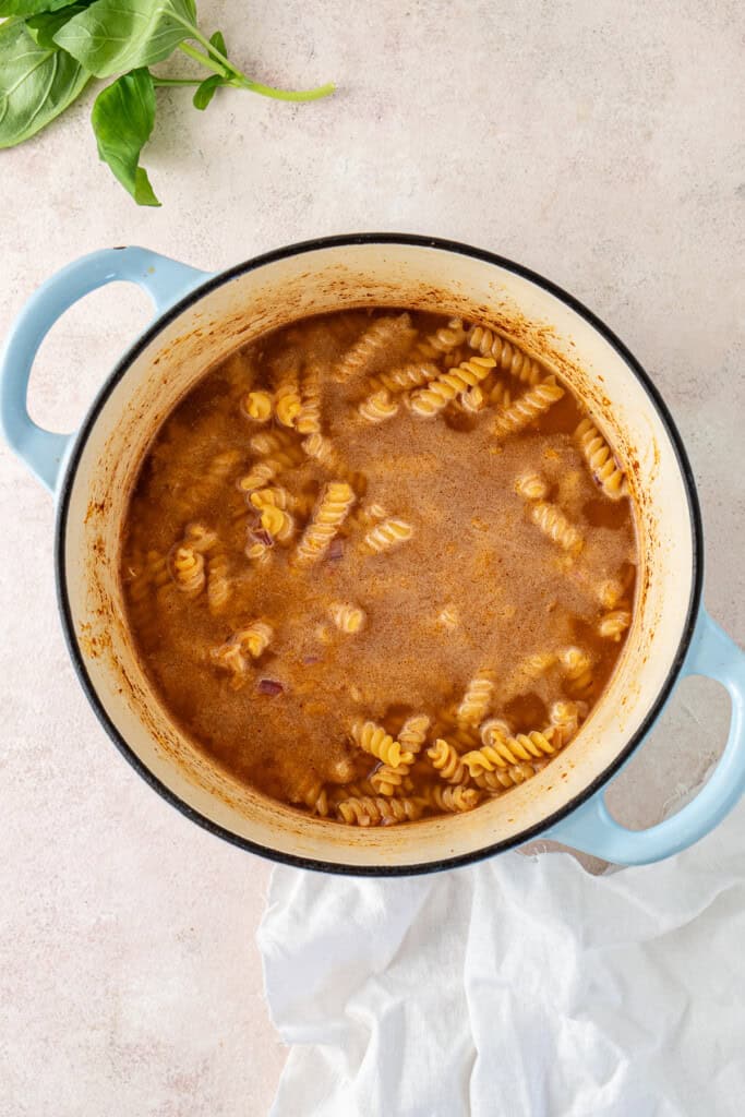 Adding the pasta and chicken stock to the pot.