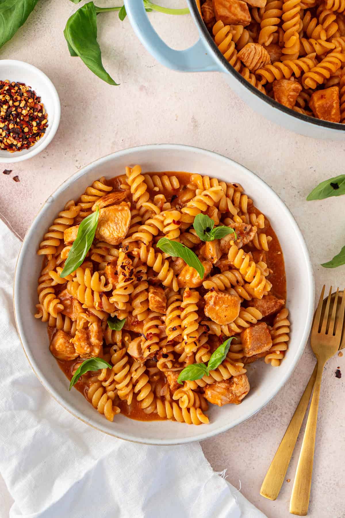 One pot creamy Tomato chicken pasta served into bowls topped with basil and chilli flakes.