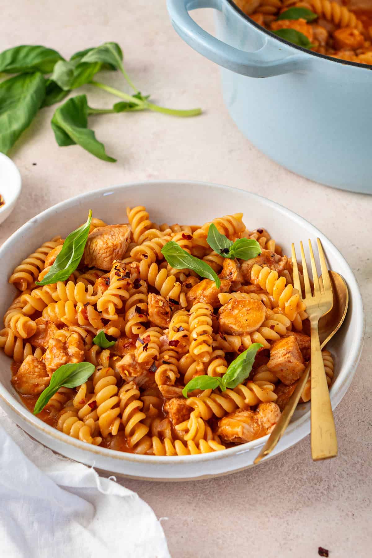 Dairy free tomato chicken pasta in a bowl with fresh basil.