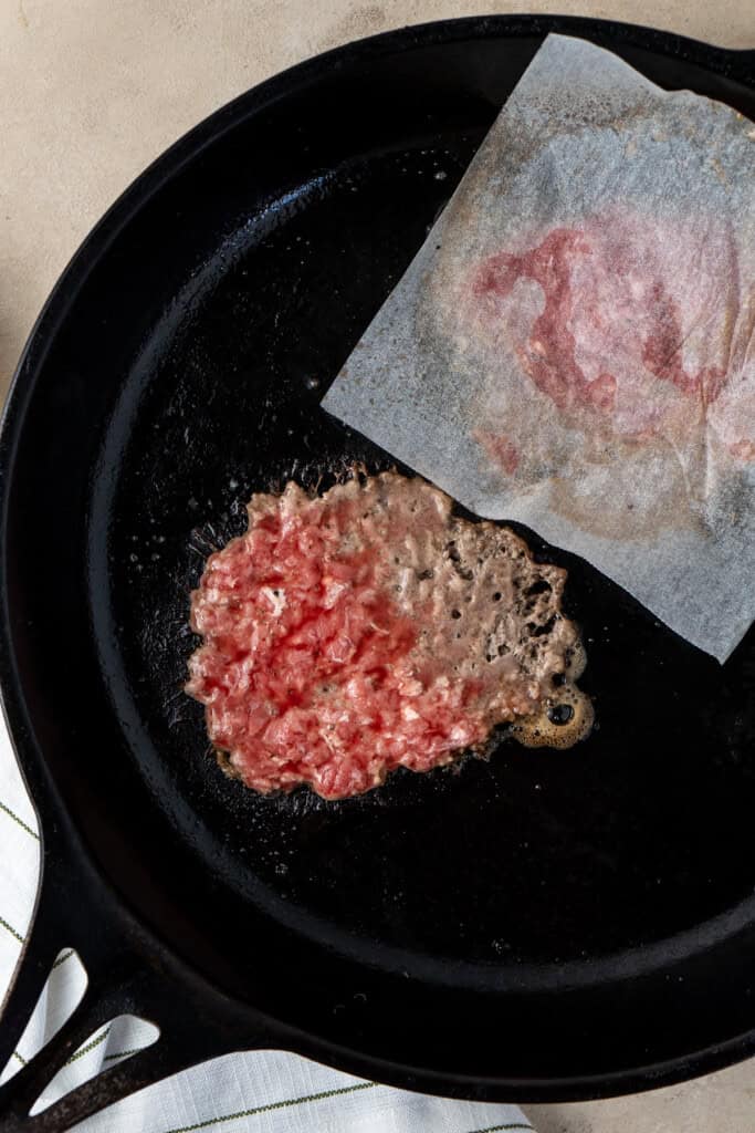 Smashing the meat in a cast iron pan.