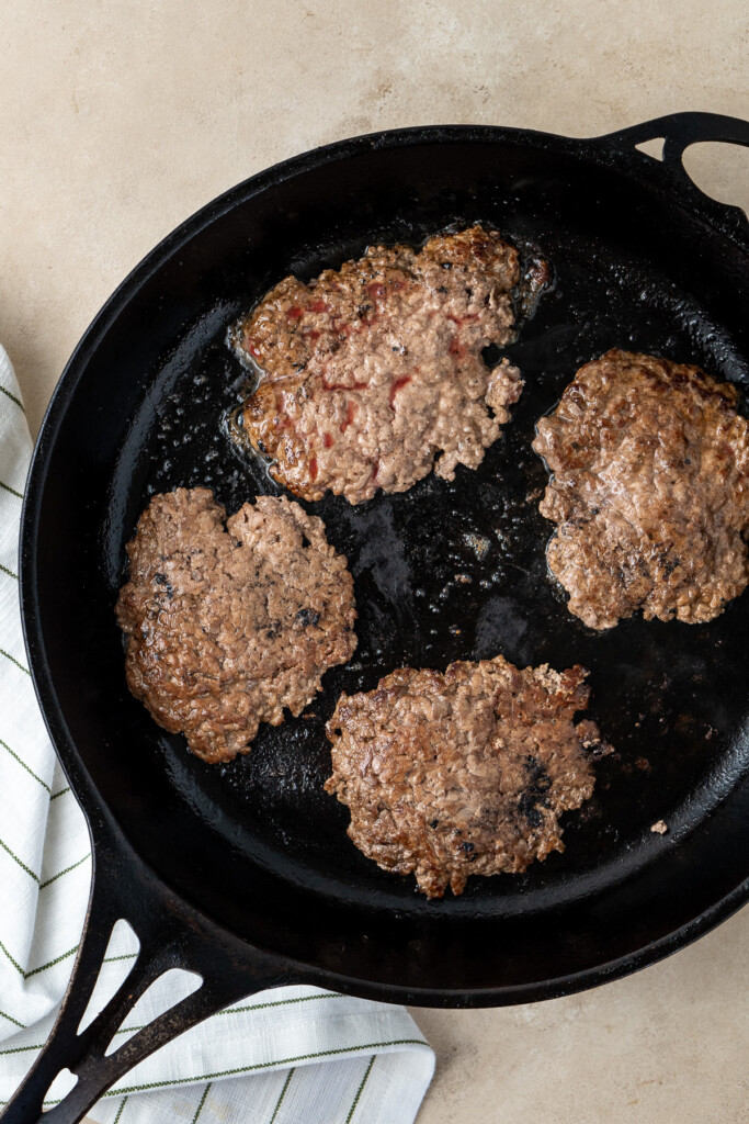 The burger patties in a cast iron pan.