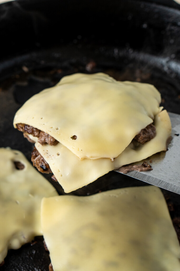 Double stacking the burger patties with cheese on a spatula. 