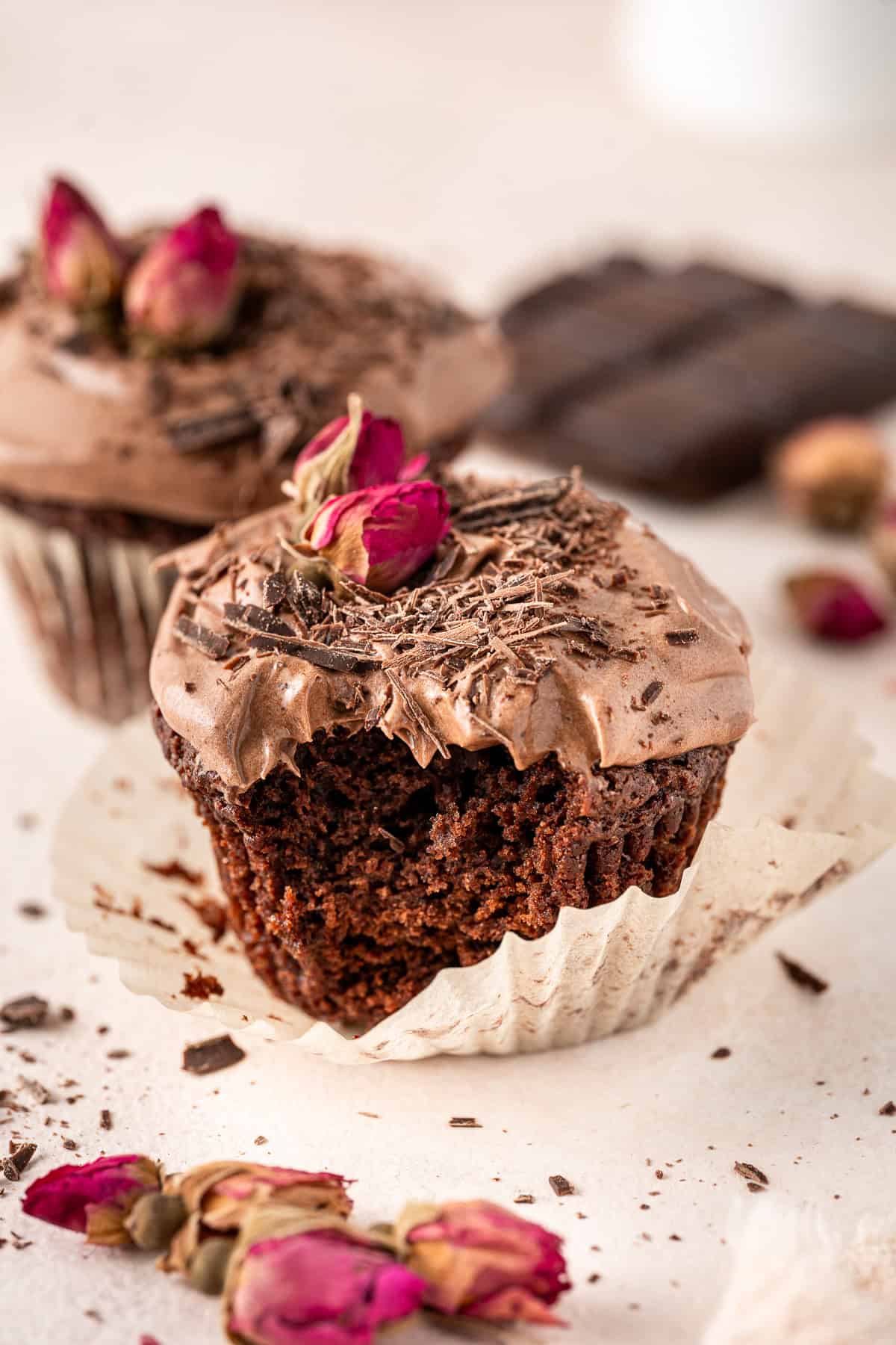 Close up of the chocolate cupcake with a bite taken, decorated with dried roses. 