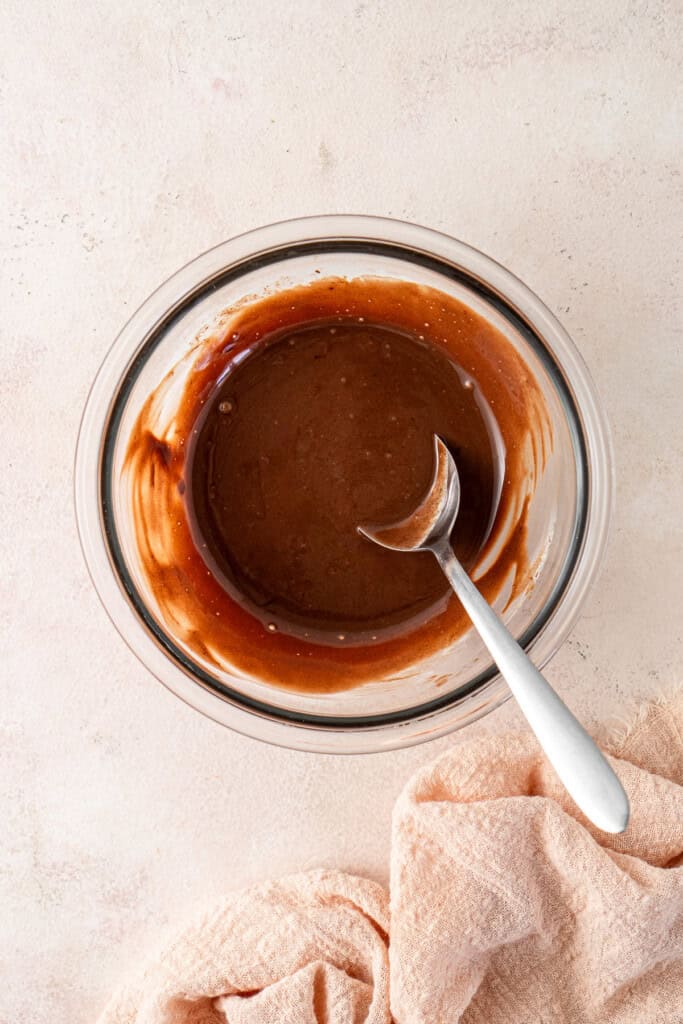 The glossy chocolate ganache in a small bowl with a spoon.