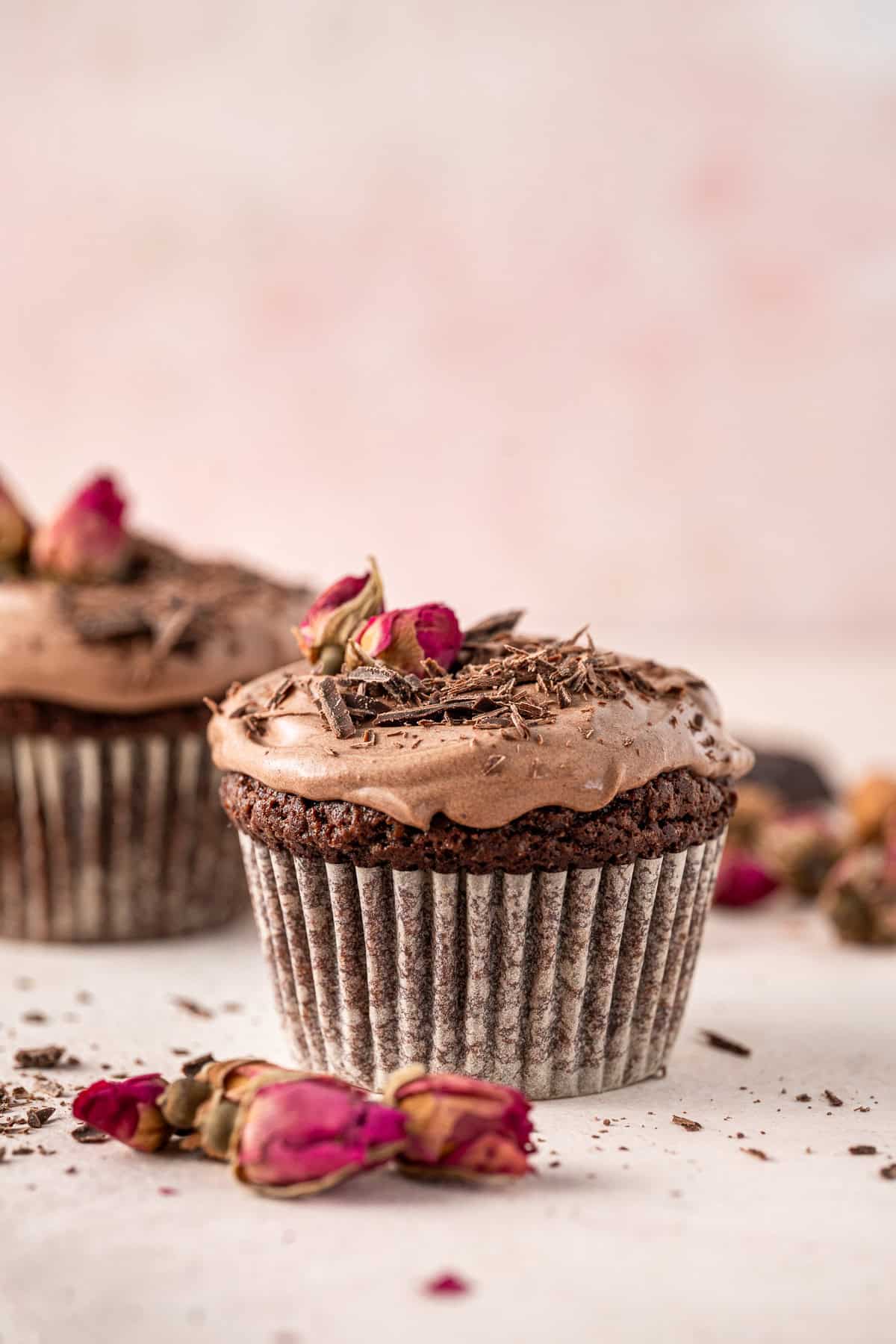 Two dairy free chocolate cupcakes topped with whipped ganache and dried roses.