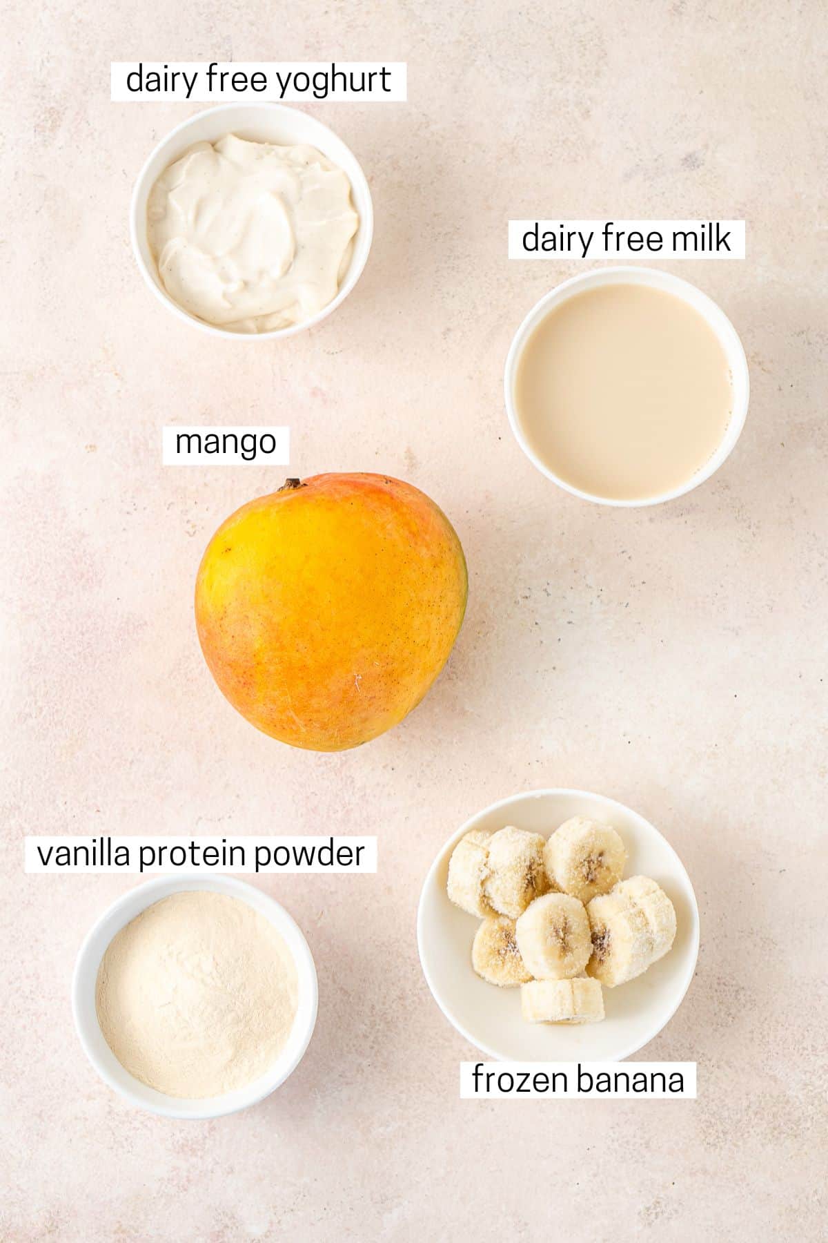 All ingredients needed to make a mango smoothie laid out in bowls.