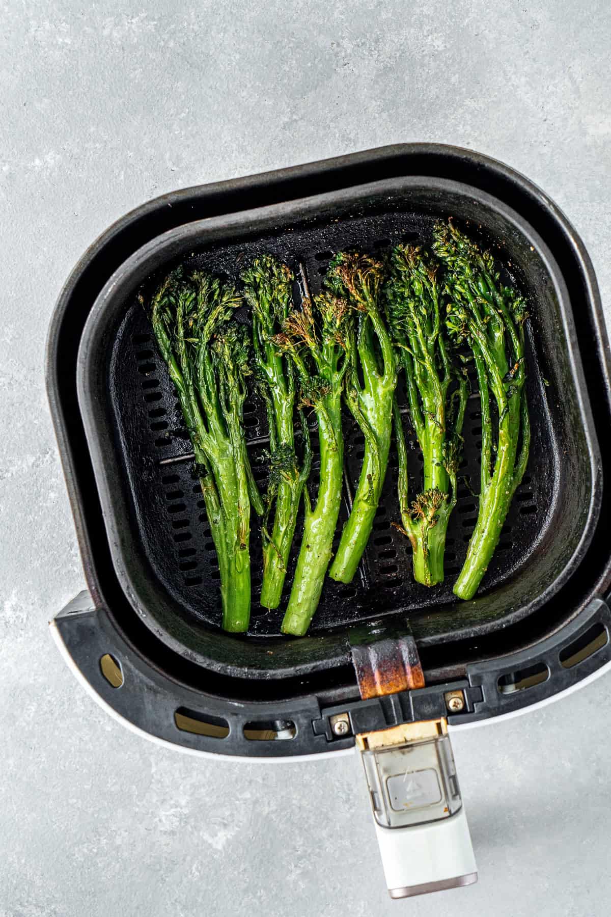 Cooked broccolini in the air fryer basket.