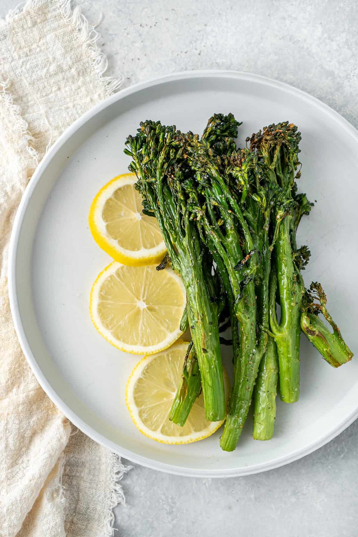 Air fryer broccolini served onto a white plate with lemon. 