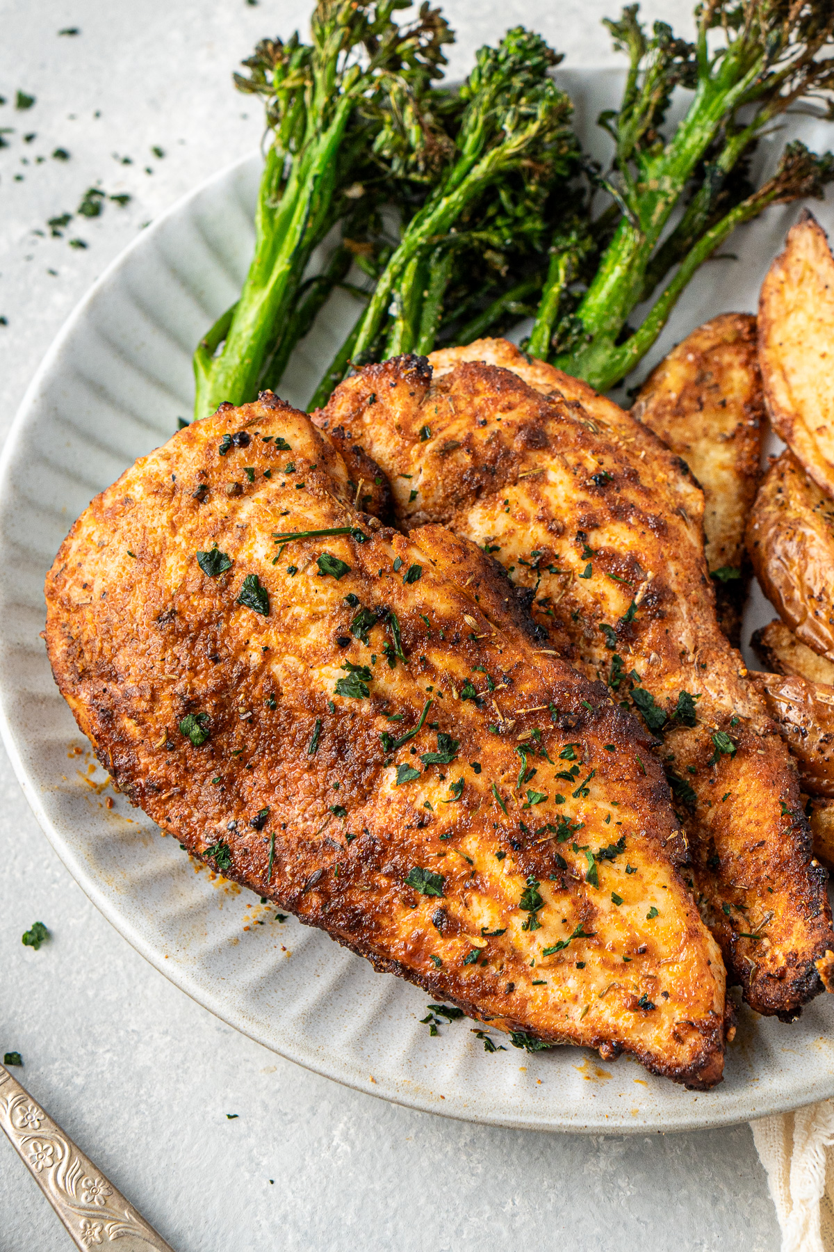 Close up of cooked air fryer chicken breast on a plate with potatoes and broccolini.