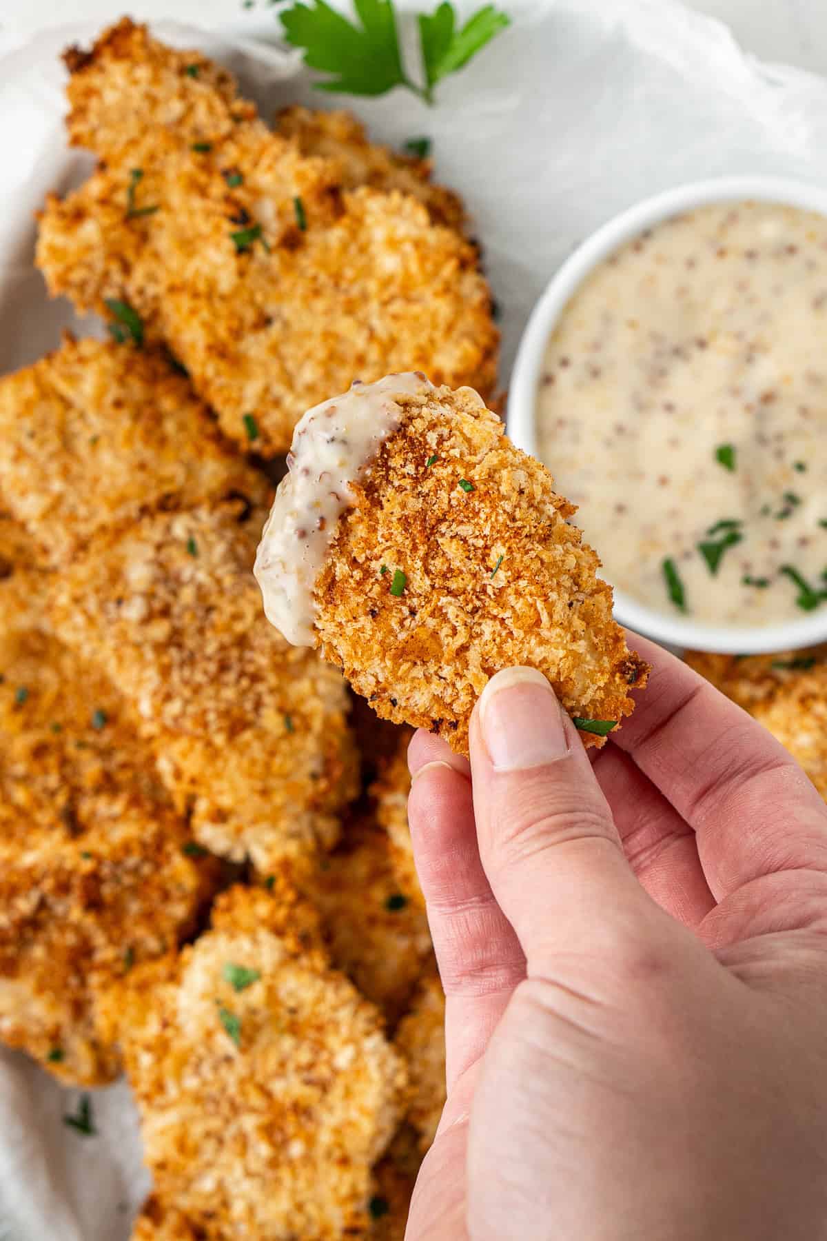 A hand holding a chicken nugget dipped in honey mustard sauce.