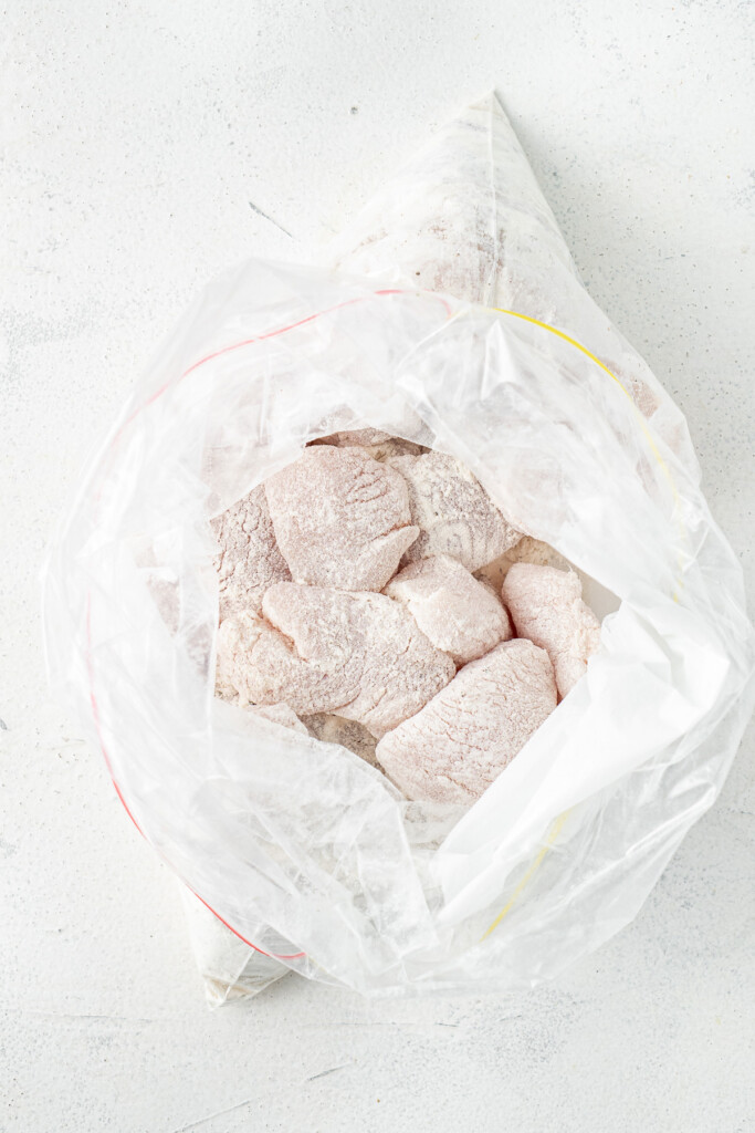 Chicken pieces in a plastic bag coated with flour.