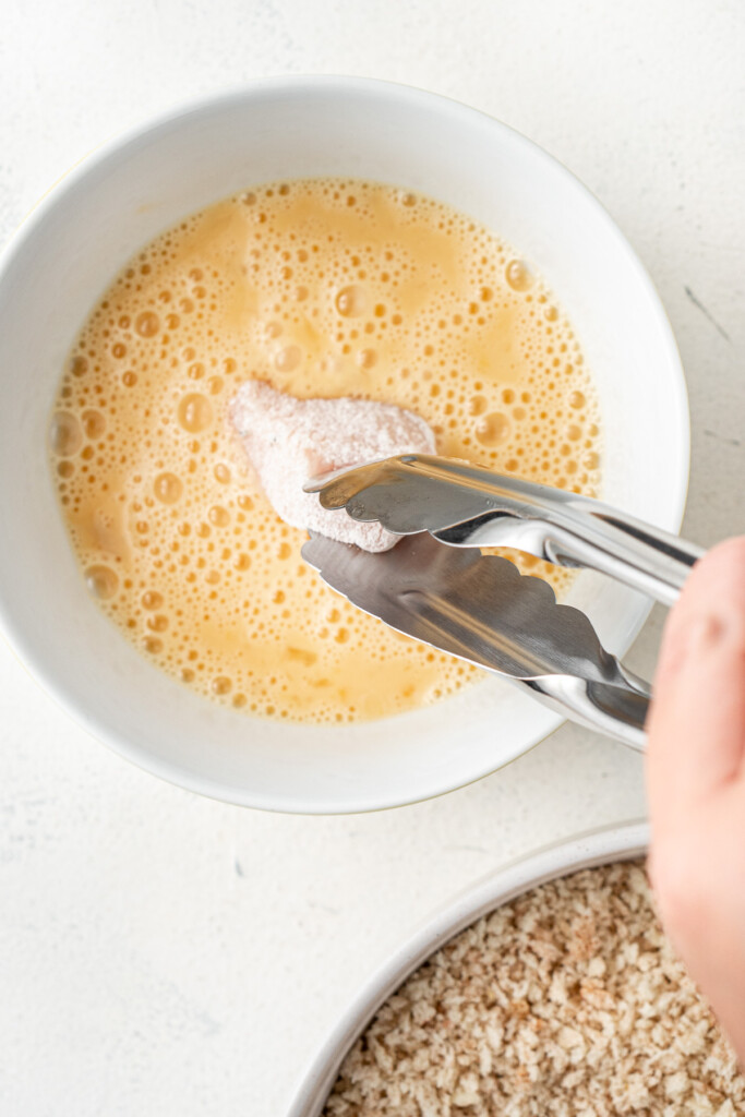 Dipping the nugget in the egg mixture.