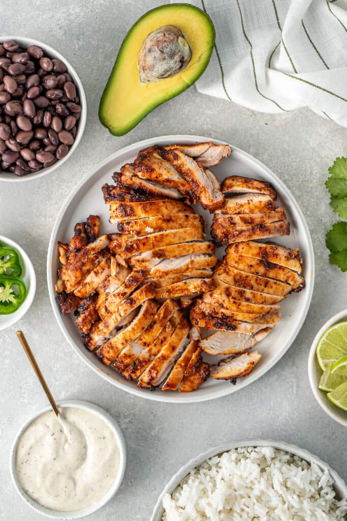 The sliced chicken thighs on a plate with other ingredients around it.