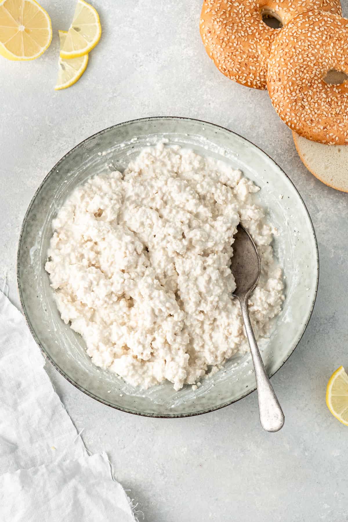Dairy free cottage cheese in a bowl with a spoon with bagels in the background.