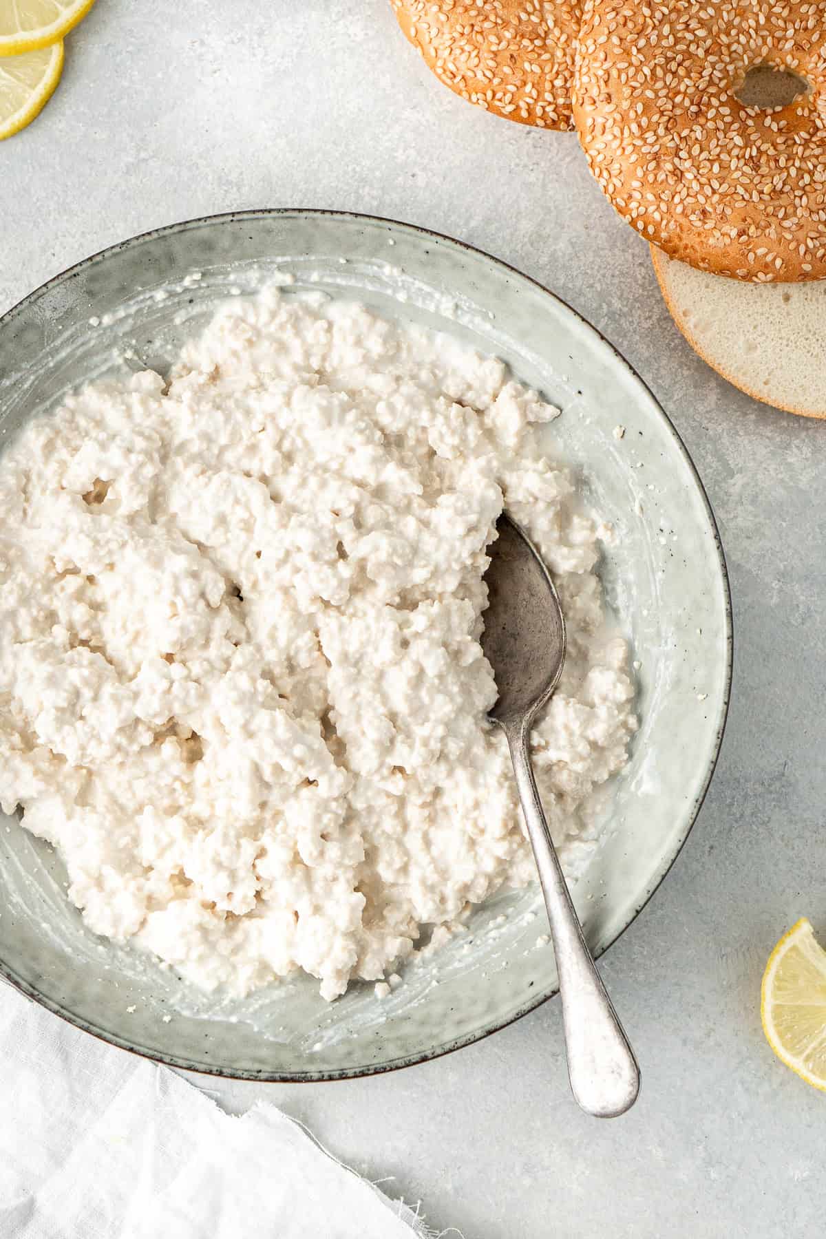 Close up of cottage cheese in a bowl with lemons and bagels on the side.