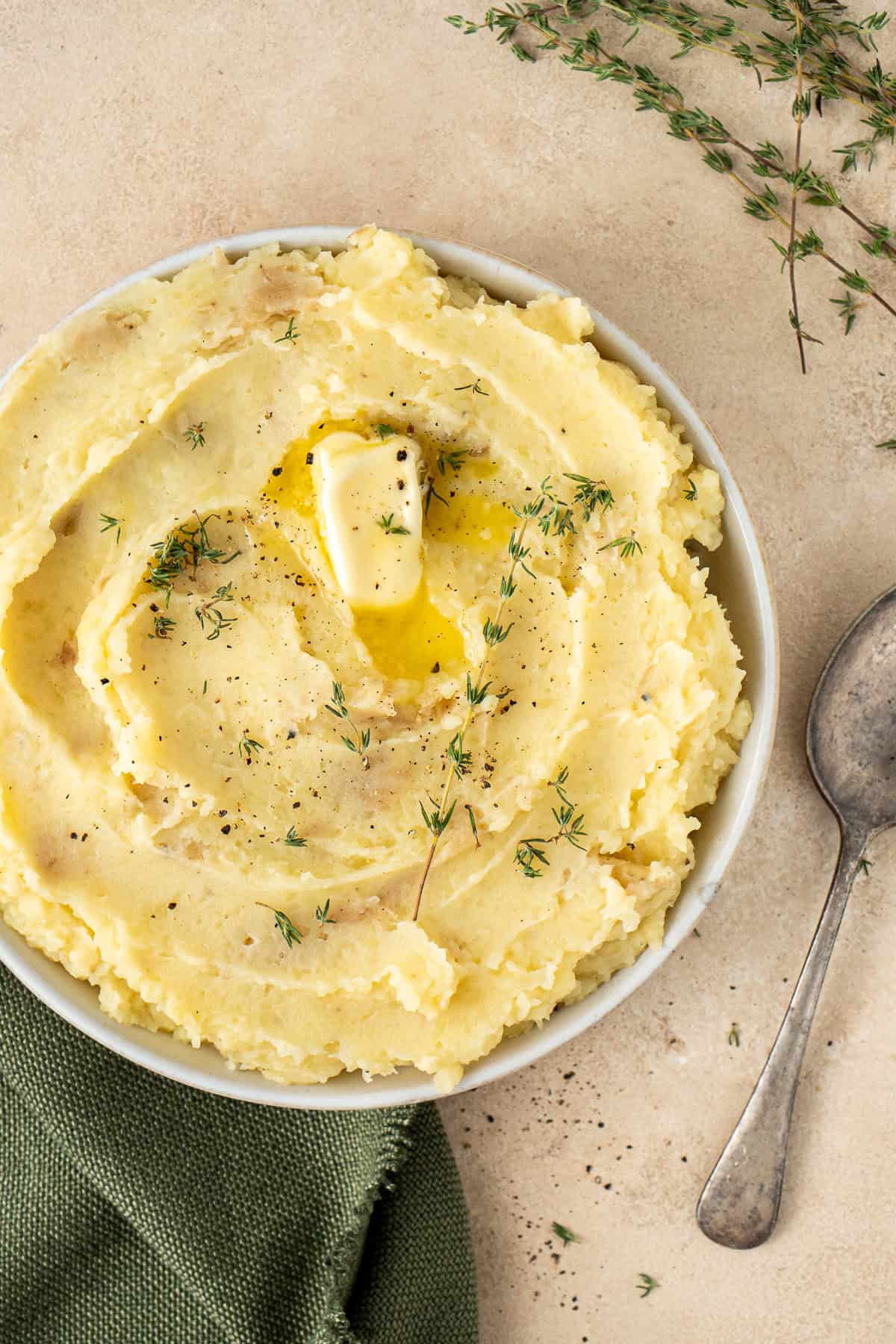 Close up of mashed potatoes in a bowl with butter and thyme.