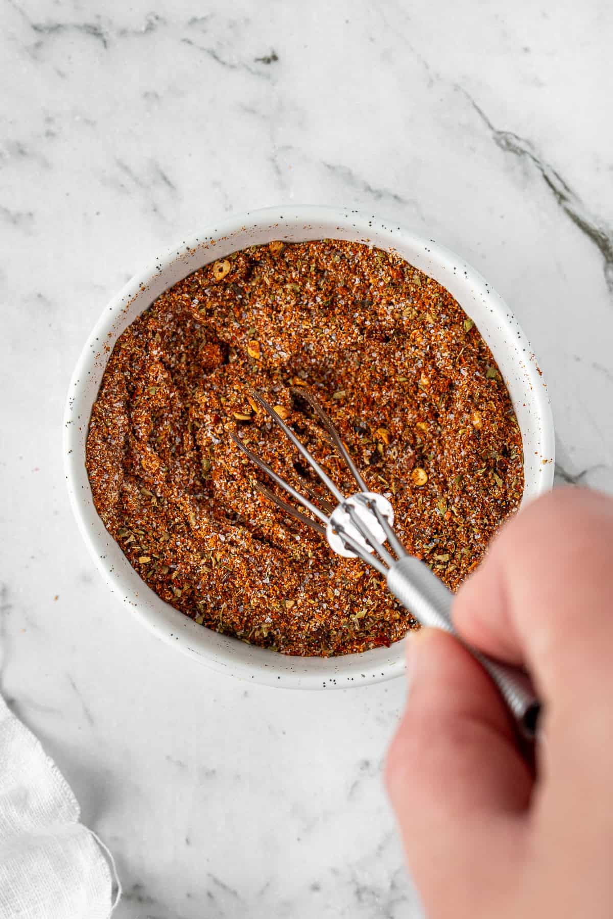 A hand whisking together all of the spices in a small bowl.