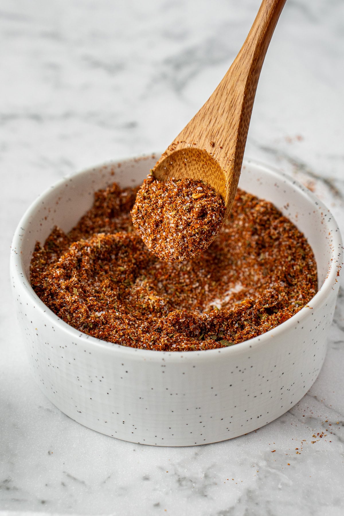 A spoon scooping out some of the taco seasoning blend from a small bowl.