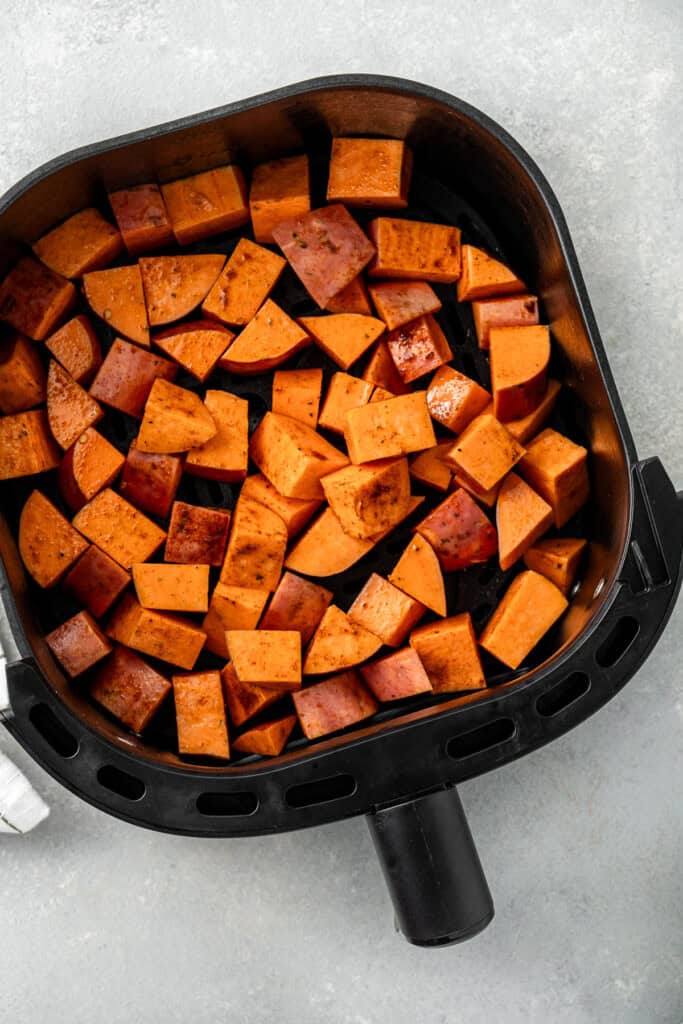 Raw sweet potatoes in the base of a air fryer basket.